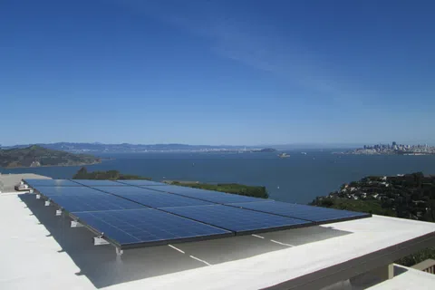 Solar panels installed on a rooftop overlooking a bay with a city skyline in the background under a clear blue sky.