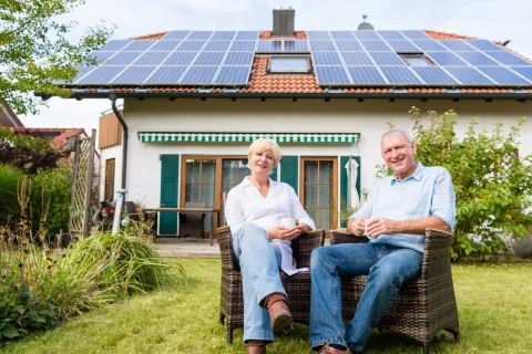 a man and woman sitting on a bench in front of a house
