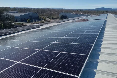 Large array of solar panels installed on a metal rooftop under clear blue sky with distant hills.