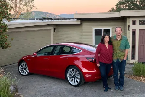 a man and woman standing next to a red car in front of a house