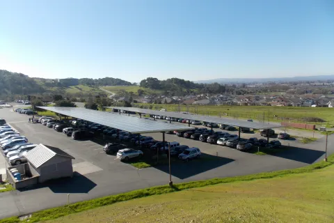 Parking lot with solar panel canopies covering rows of parked cars under clear blue sky on a sunny day.