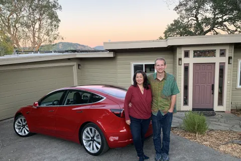 a man and woman standing next to a red car in front of a house