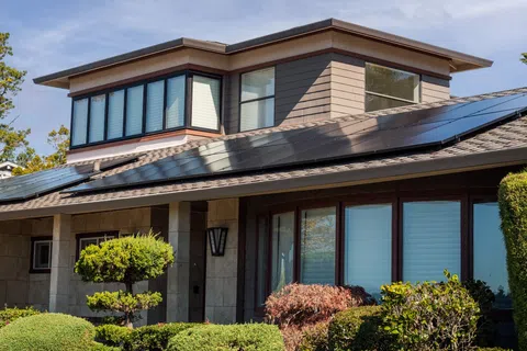 Modern house with solar panels on the roof surrounded by green shrubs and trees under a clear sky