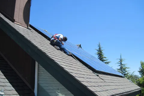 Worker installing solar panels on a sloped residential roof under a clear blue sky