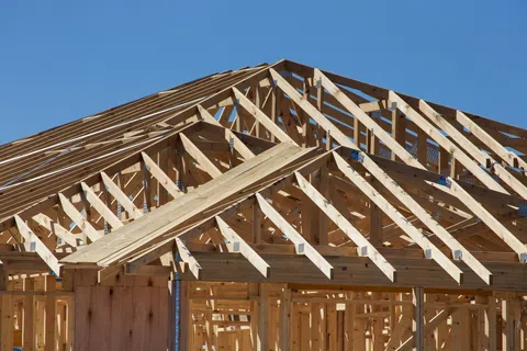 Wooden frame structure of a house under construction against a clear blue sky on a sunny day.