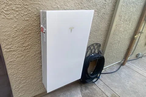 Tesla Powerwall mounted on a wall with wiring nearby in a modern home setting.