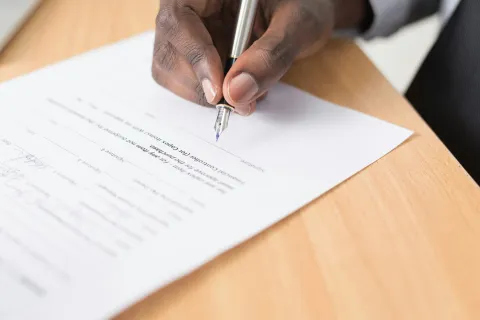 Close-up of a person signing a Managed IT provider contract with a silver pen on a wooden table