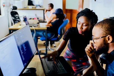 Two local IT service providers collaborating at a laptop in an open office space.