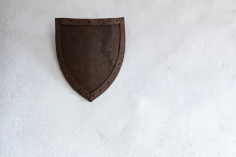 Rusty medieval metal shield with rivets mounted on a plain white textured wall referencing Guardian IT