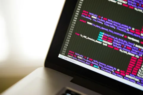 Close-up of laptop screen displaying colorful lines of computer code representing the threat of cyberattacks.