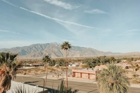 Desert townscape with palm trees, clear sky, and mountain range in the background under bright daylight.