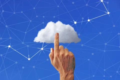 Hand pointing at a cloud icon with a blue network background, symbolizing cloud computing and data connectivity.