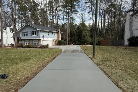 Newly poured concrete driveway leading to a two-story house with surrounding lawn and tall trees.