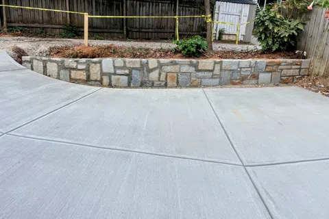 New concrete driveway with decorative stone retaining wall and wooden fence in backyard space.
