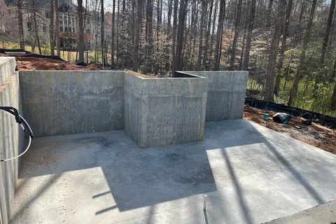 Concrete foundation walls and slab for a new house under construction in a wooded residential area.