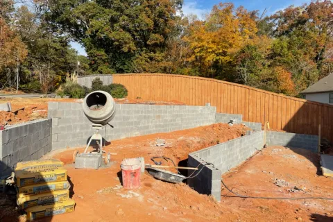 Construction site showing a cement mixer, block wall foundation, and autumn landscape in the background.