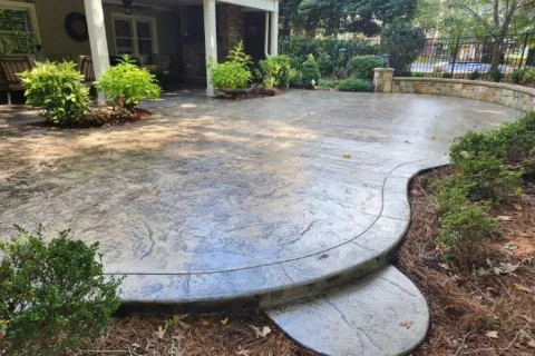 Stylish stamped concrete patio with lush greenery and smooth curves, perfect for outdoor relaxation.