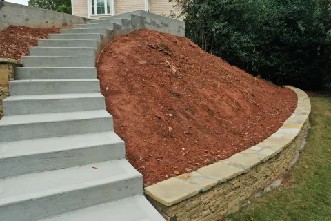Concrete stairs leading up a landscaped hill, surrounded by stone retaining walls and greenery.