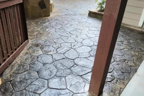 Decorative stamped concrete path with a textured stone pattern, surrounded by greenery and a wooden fence.