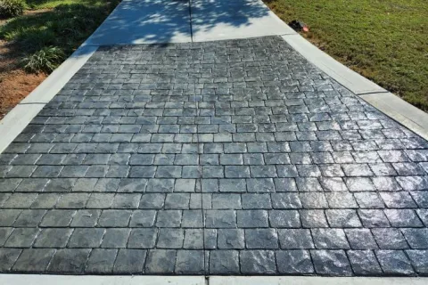Stamped concrete driveway with a textured stone pattern and smooth concrete border under sunlight.