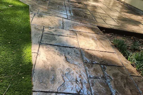 Beautifully stamped concrete pathway with a glossy finish, surrounded by green grass and sunlight.