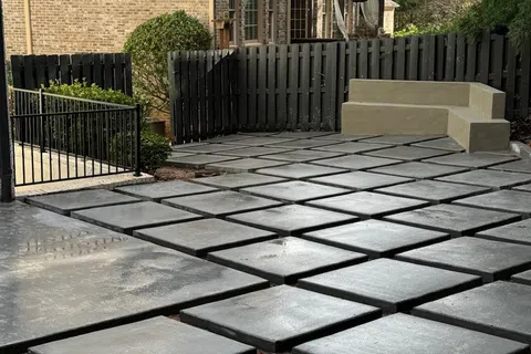 Modern outdoor patio with large square concrete pavers and built-in concrete bench seating near a black fence.