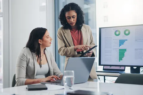 Two women examine data on a tablet.