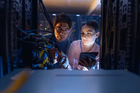 Two IT professionals inspecting server hardware and cables inside a data center rack using a tablet.