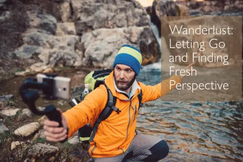 Man in orange jacket and blue hat vlogging by rocky stream in nature setting