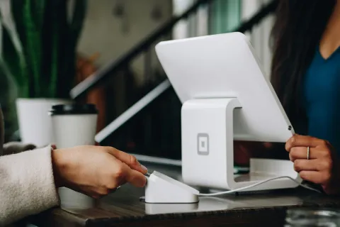 Person making a payment using a card reader at a small business modern white point-of-sale terminal showing that small businesses need cybersecurity.