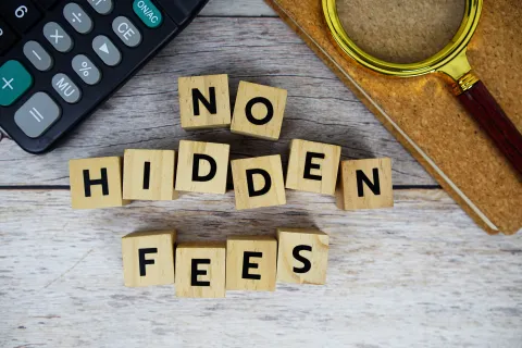 Wooden blocks spelling No Hidden Fees with calculator, notebook, and magnifying glass on wooden surface.