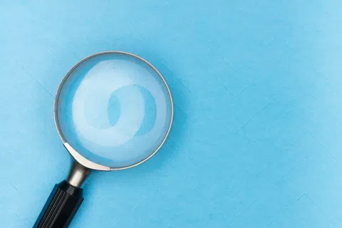 Magnifying glass with black handle on a blue textured background focusing light reflection.