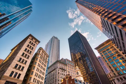 Skyscrapers and historic buildings converging toward a clear blue sky with light clouds in a city skyline.