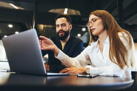 Two professionals collaborating over a laptop in a modern office setting with focused expressions.