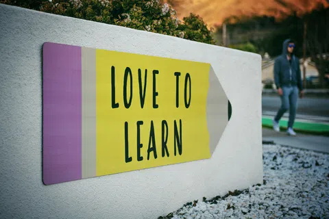 Large pencil-shaped sign on white wall with message Love to Learn in black text outdoors