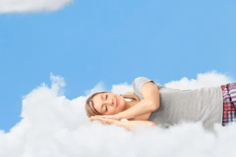 Woman peacefully sleeping on a fluffy white cloud against a bright blue sky with scattered clouds