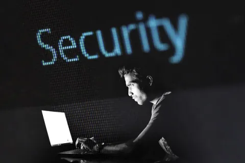 Focused man works on laptop with large glowing Security text in dark background highlighting cybersecurity.