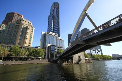 Cityscape with river, modern high-rise buildings, and a pedestrian bridge over the water on a clear sunny day