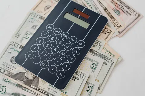 Black solar-powered calculator placed on a spread of US dollar bills of various denominations on a white surface.