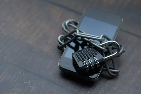 Smartphone secured with metal chain and combination lock on wooden surface symbolizing digital security.