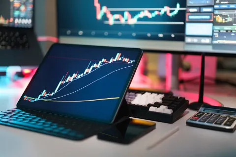 Tablet displaying upward stock chart with candlesticks on desk alongside keyboard and calculator.