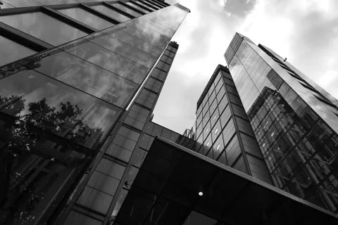 Low-angle black and white photo of modern glass skyscrapers with reflections and cloudy sky.