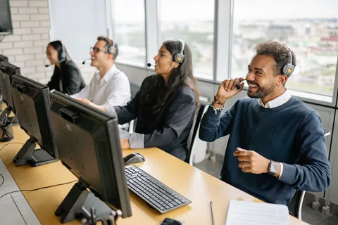 Customer service team wearing headsets working on computers in a bright office with large windows.