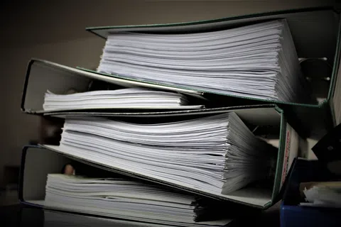 Stack of thick binders filled with numerous white printed documents on a dark background