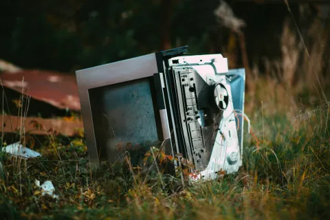 Broken computer lying in tall grass outdoors after a natural disaster.