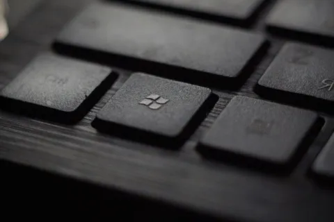 Close-up of a black keyboard with a Windows logo key in focus on a wooden surface.