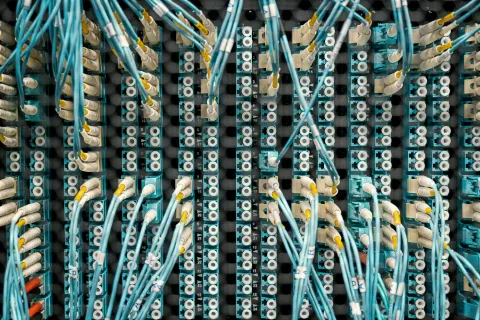 Close-up of network fiber optic cables connected to blue patch panels in a data center rack.