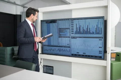 Businessman in suit analyzing financial data and charts on a large screen in modern office conference room.