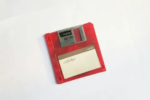 Red 3.5-inch floppy disk with a handwritten date label on a white background showing how outdated tech isn't helpful