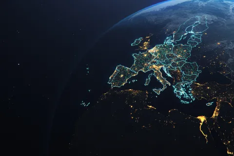 Satellite view of Europe at night showing illuminated cities and country borders with a glowing blue outline.